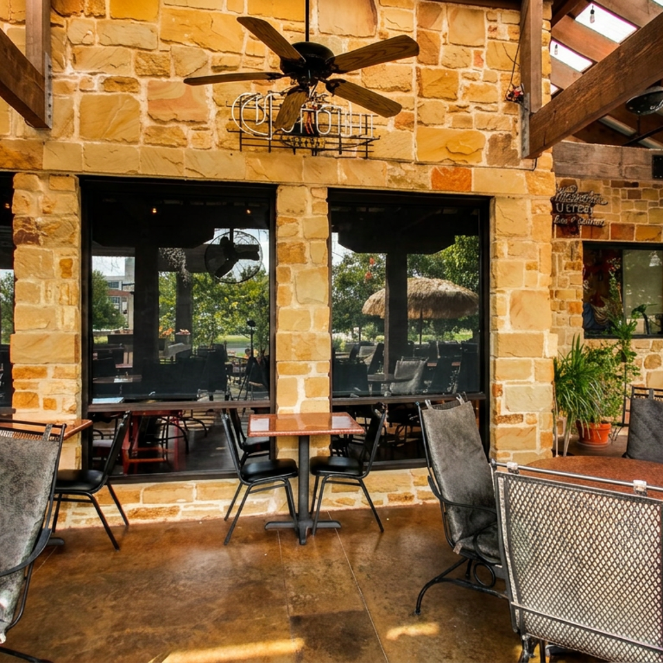 Outdoor patio with stone walls, ceiling fans, and tables with chairs, overlooking a green landscape.