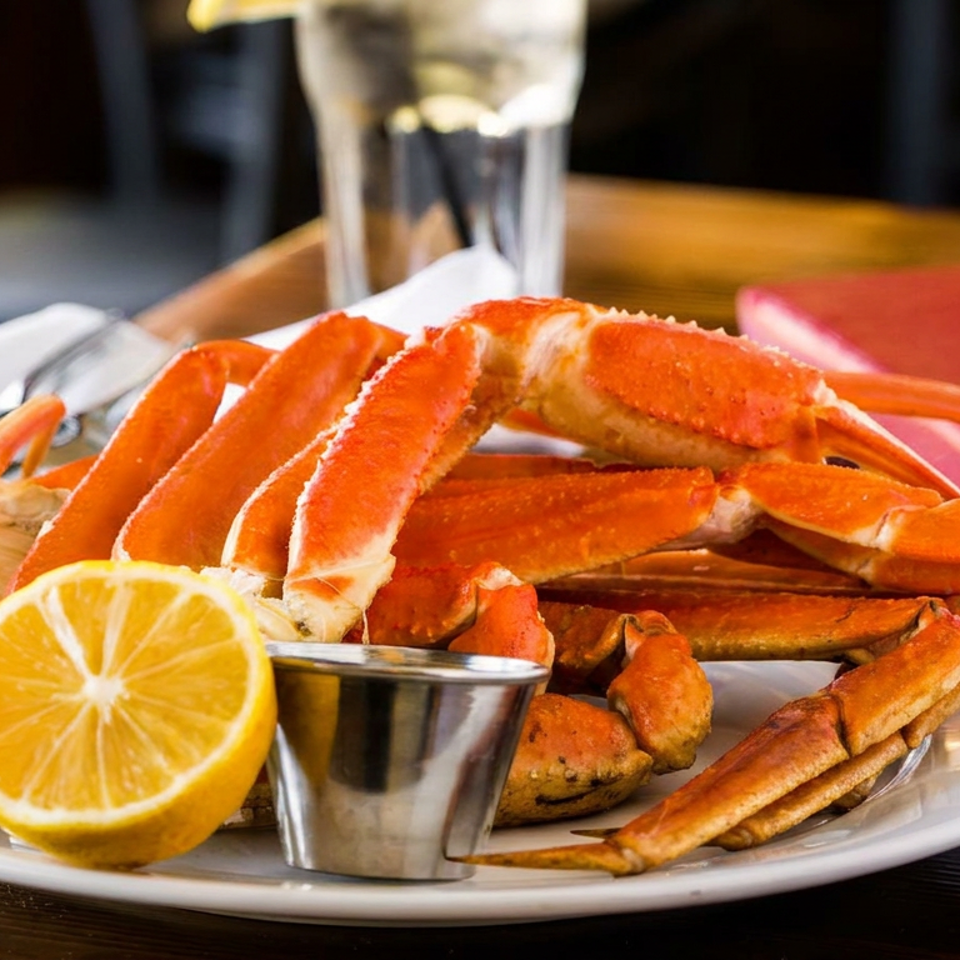 A plate of cooked crab legs with a lemon half and dipping sauce on a wooden table.