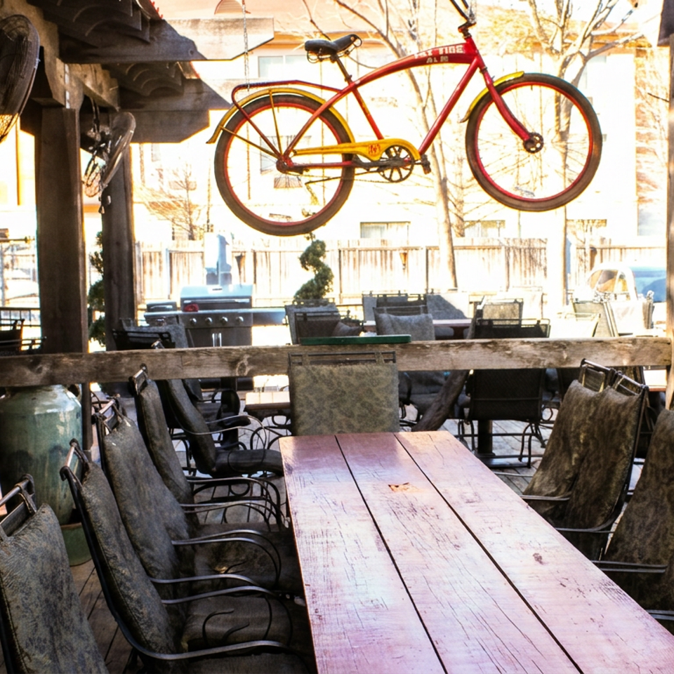 Outdoor patio dining area with a long wooden table, chairs, and a red bicycle hanging overhead.
