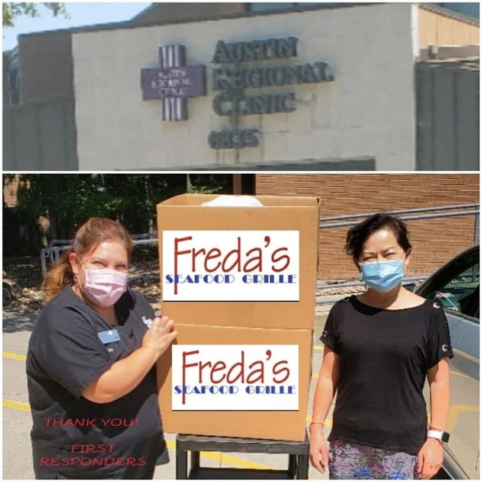 Two masked women stand beside a Freda’s Seafood Grille sign outside Austin Regional Clinic, thanking first responders.