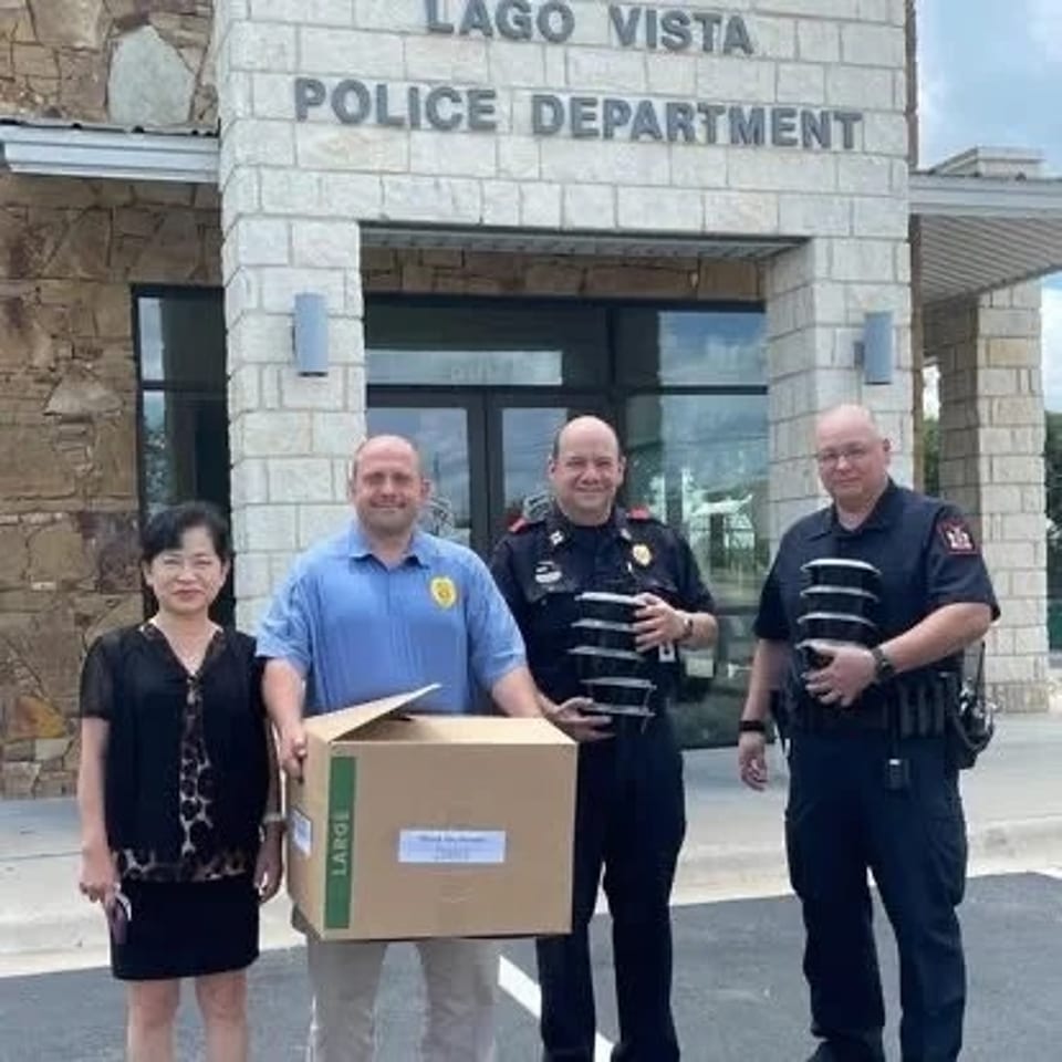 Four people stand outside the Lago Vista Police Department, with officers holding a large cardboard donation box.
